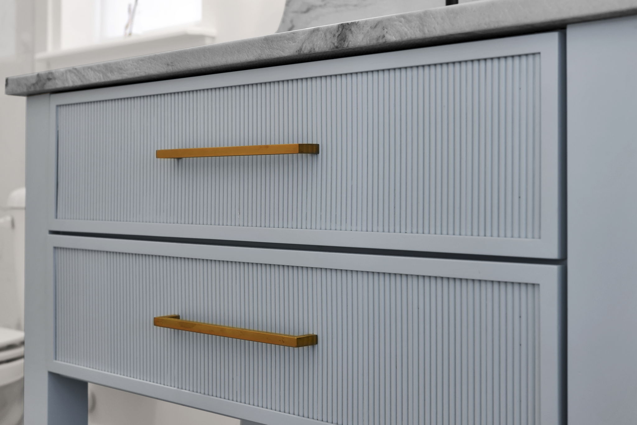 Close-up of a blue reeded vanity with brass hardware in a completed bathroom